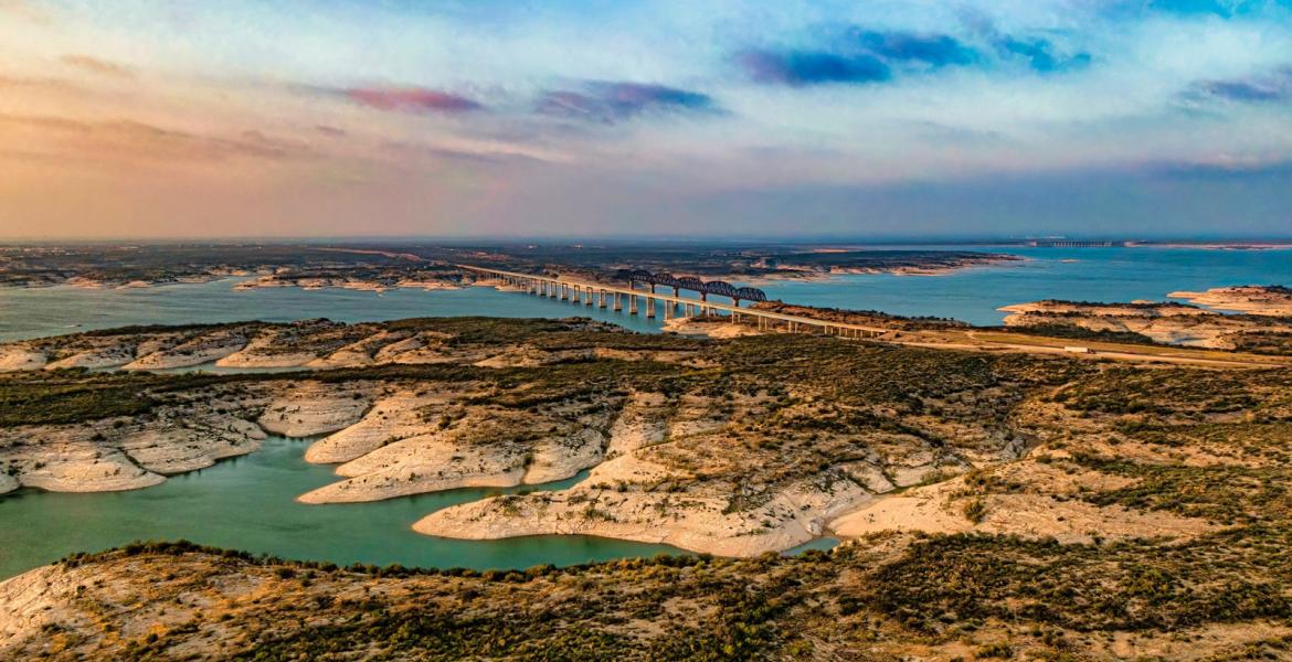 Aerial view of Amistad Reservoir with the Governor's Landing Bridge in Del Rio, Texas at sunset. Fed by the Rio Grande, Devils River, and Pecos River, water levels at Lake Amistad have been low for over a decade.